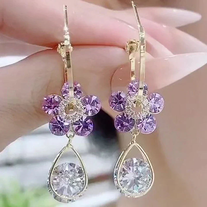 Goldene Ohrringe mit lila Blumen und klaren Tropfenanhängern, funkelnd, elegant, Schmuck.