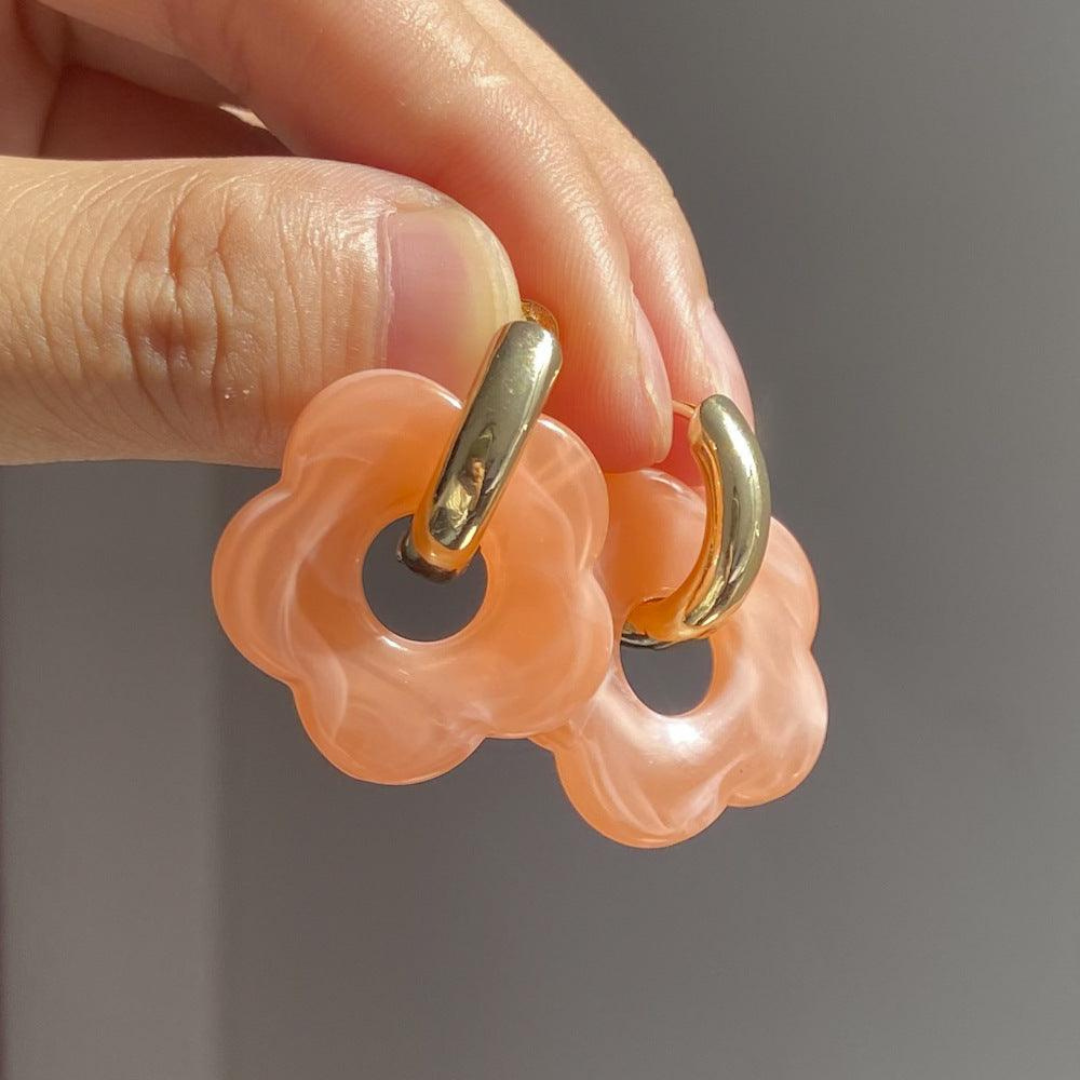 Hand hält goldene Creolen mit rosa Blumenanhängern, modische Ohrringe, Schmuckaccessoire.