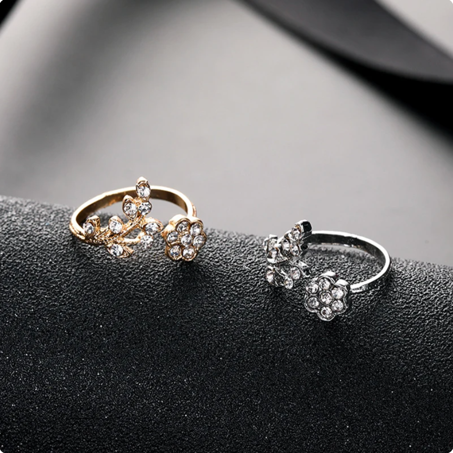 Zwei elegante Blumenringe, gold und silber, mit funkelnden Kristallen auf schwarzem Hintergrund.