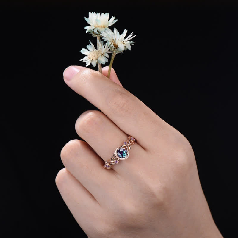 Hand mit Blumenstrauß und roségoldenem Ring mit blauem Edelstein auf schwarzem Hintergrund.