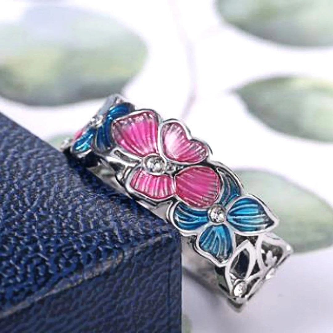 Silberring mit rosa und blauen Blumen, Kristallsteinen, auf blauem Hintergrund.