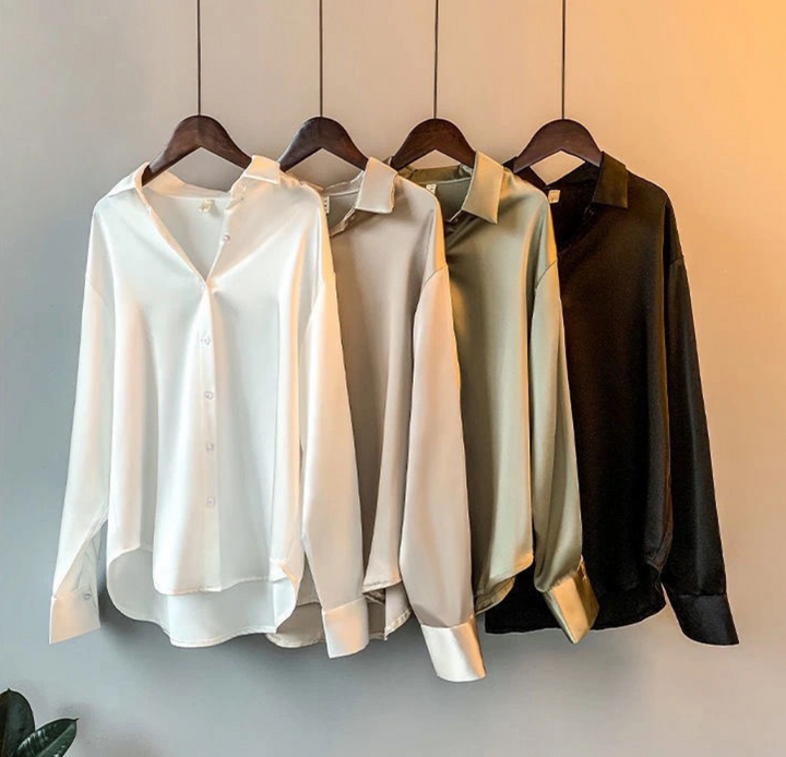 Vier elegante Damenblusen auf Kleiderbügeln, in Weiß, Beige, Grün und Schwarz.