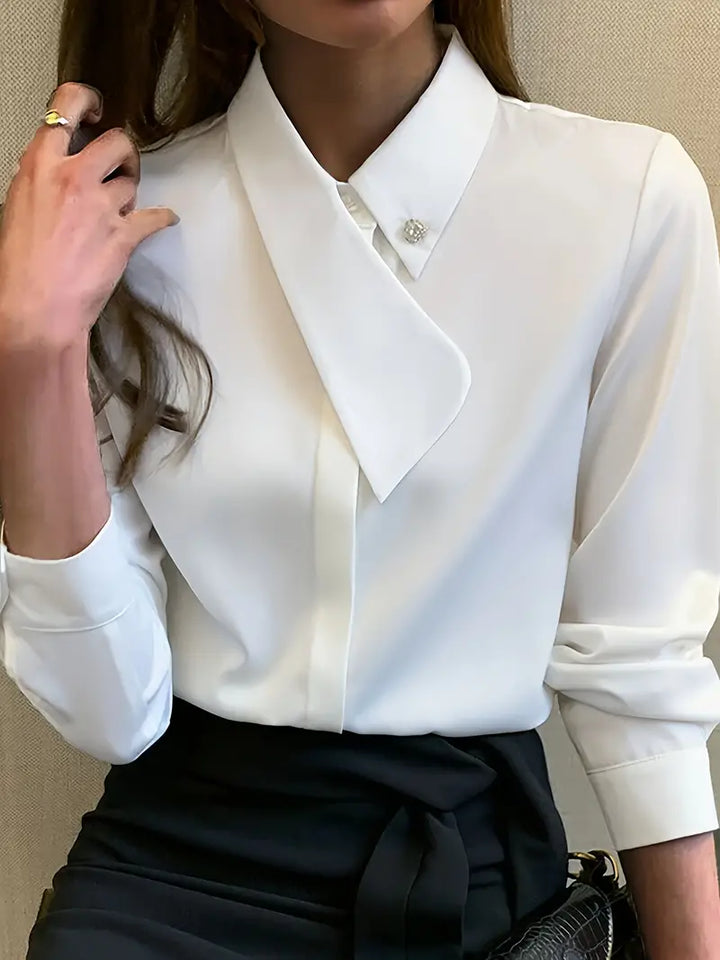 Frau in weißer Bluse mit asymmetrischem Kragen, schwarze Hose, eleganter Business-Look.