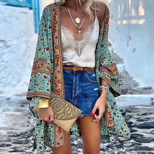 Frau in Boho-Kimono, blau-rot gemustert, mit Jeansshorts und goldener Clutch auf gepflasterter Straße.