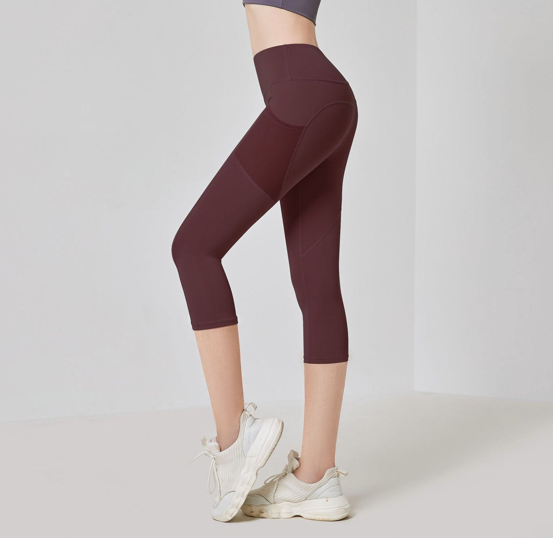 Frau in bordeauxroter Sportleggings, knielang, mit weißen Turnschuhen, seitliche Ansicht.