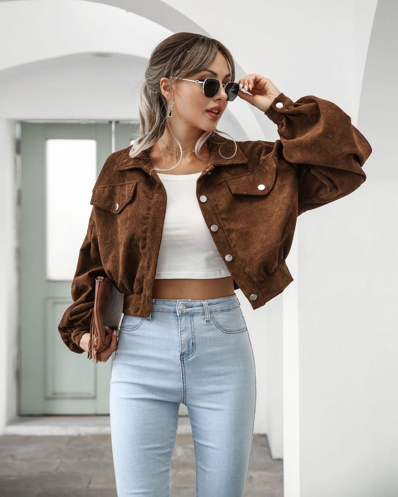Frau in brauner Cordjacke, weißem Top und blauer Jeans, modisch, lässig, Sonnenbrille.