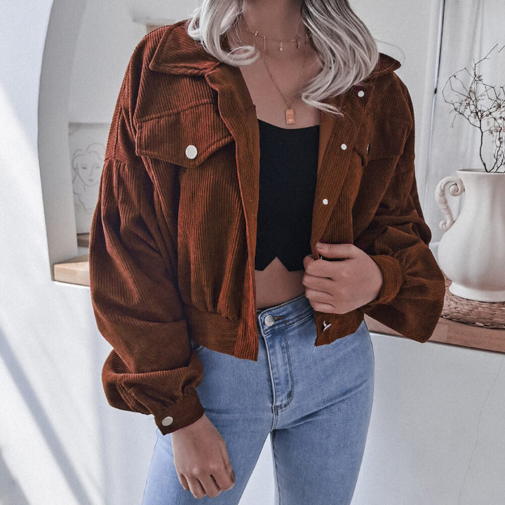 Frau in brauner Cordjacke, schwarzem Top und blauer Jeans in modernem Raum.