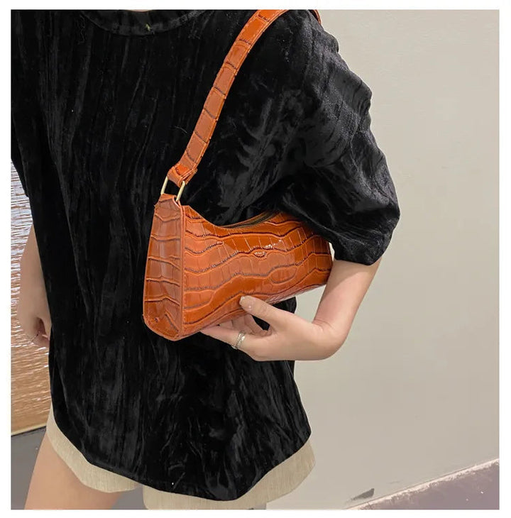 Frau mit brauner Krokodilleder-Handtasche, schwarzem Samtoberteil, modisch, elegant.