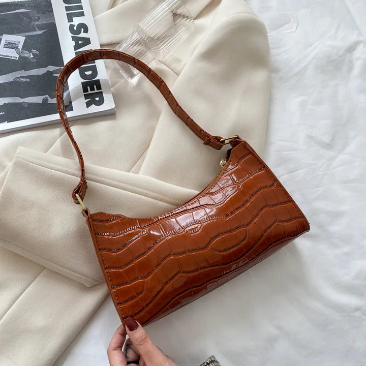 Braune Handtasche aus Krokodillederimitat auf weißem Hintergrund, modisch und elegant.