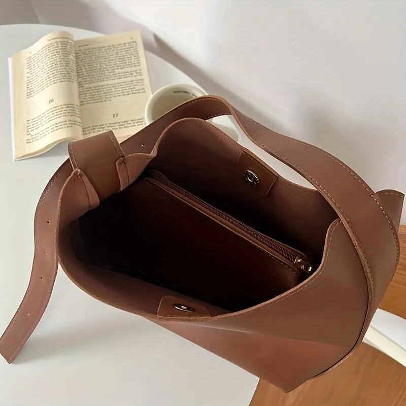 Braune Ledertasche mit offenem Hauptfach, ideal für den Alltag, auf weißem Tisch.