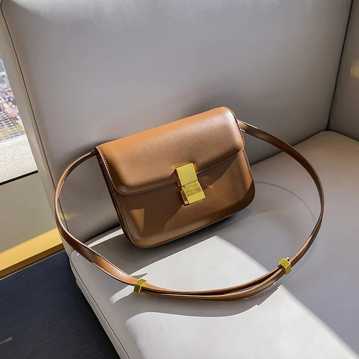 Braune Ledertasche mit goldener Schnalle auf weißem Sofa, modisches Accessoire, Damenhandtasche.
