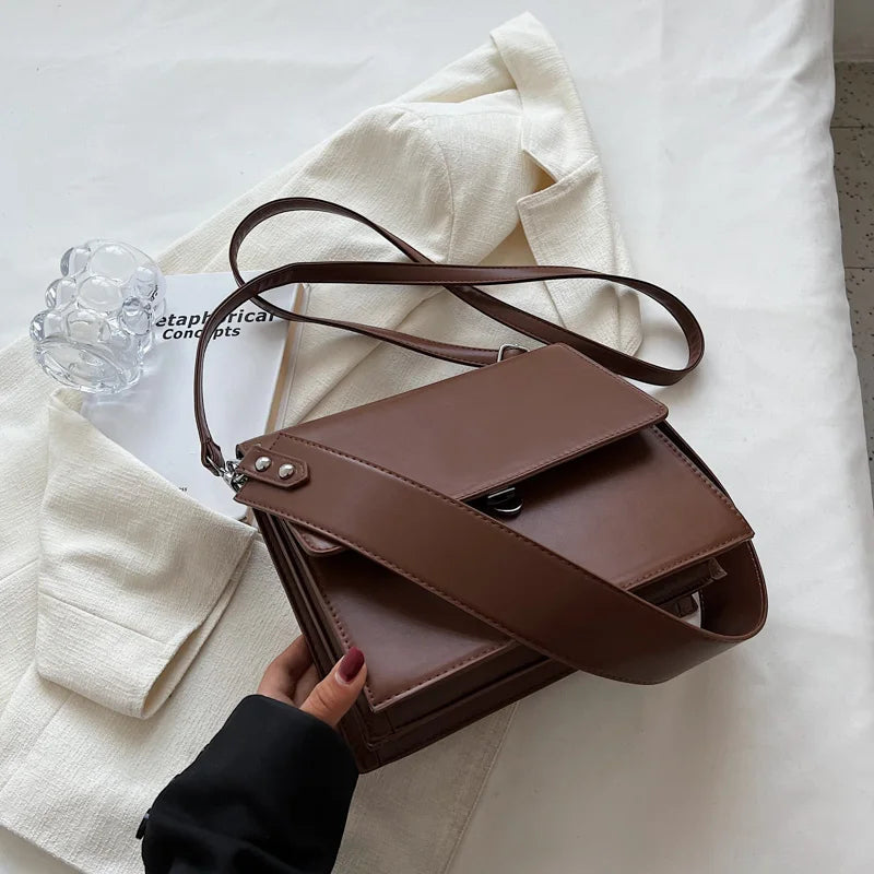 Braune Lederhandtasche mit Schulterriemen auf weißem Stoff, elegantes Design, Damenmode.