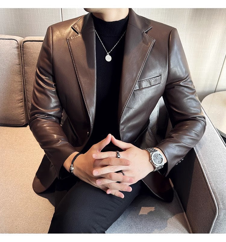 Mann in braunem Lederblazer, schwarzem Pullover, silberne Uhr, Schmuck, sitzt auf Sofa.