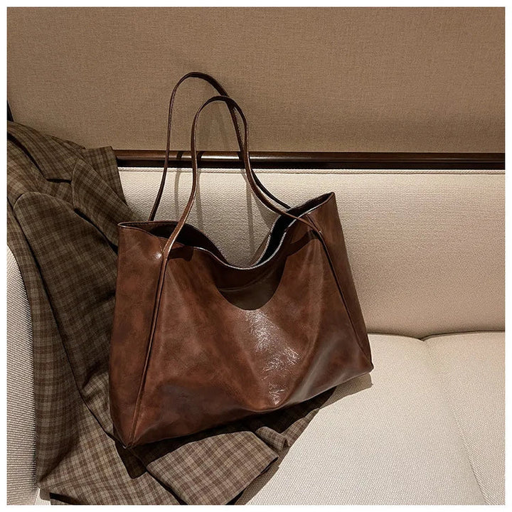 Braune Ledertasche auf kariertem Mantel, stilvoll, geräumig, für Damen, modisches Accessoire.