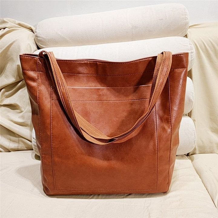 Braune Ledertasche auf beigem Sofa, langlebig, modisch, umweltfreundlich, Einkaufstasche.