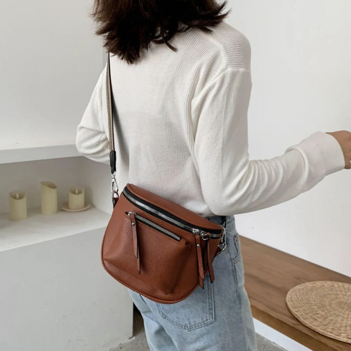 Frau mit brauner Leder-Umhängetasche, weißem Pullover, Jeans, modisch, elegant, Accessoire.