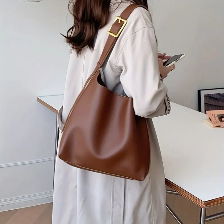 Frau mit brauner Ledertasche, Trenchcoat, Smartphone, modernes Büro, stilvolle Mode.