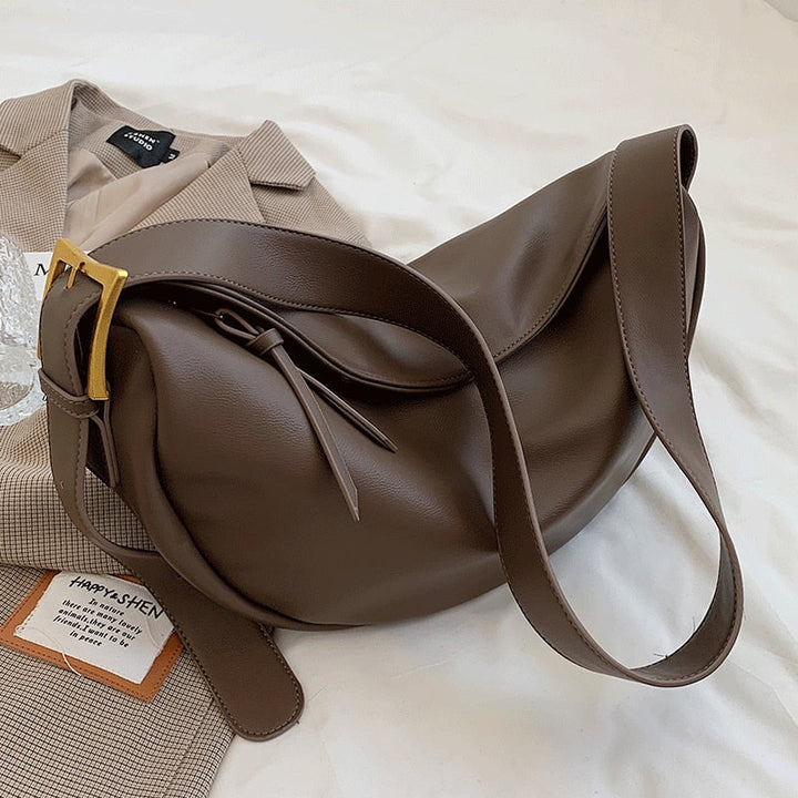 Braune Lederhandtasche mit goldener Schnalle auf beigem Blazer, modisch und elegant.