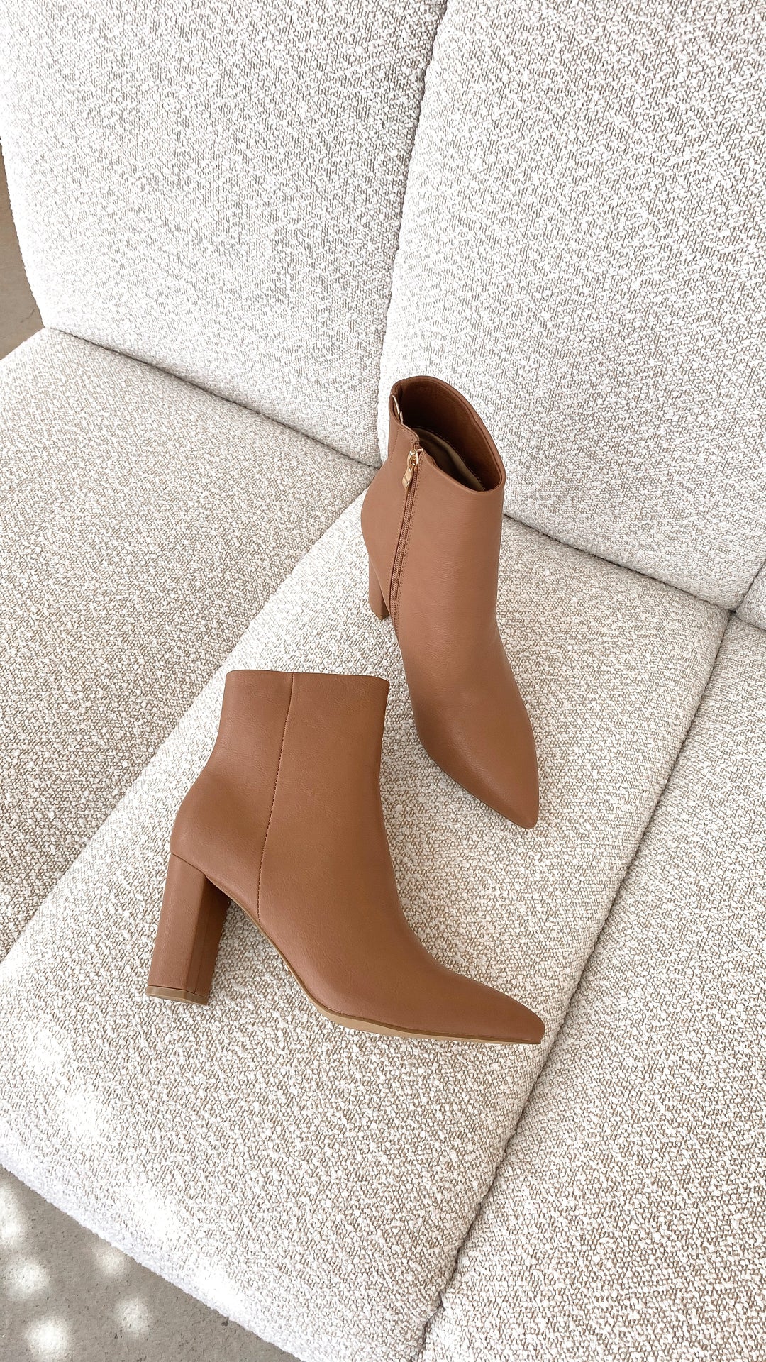 Braune Damen-Stiefeletten aus Leder mit Blockabsatz auf beigem Sofa, modisch und elegant.