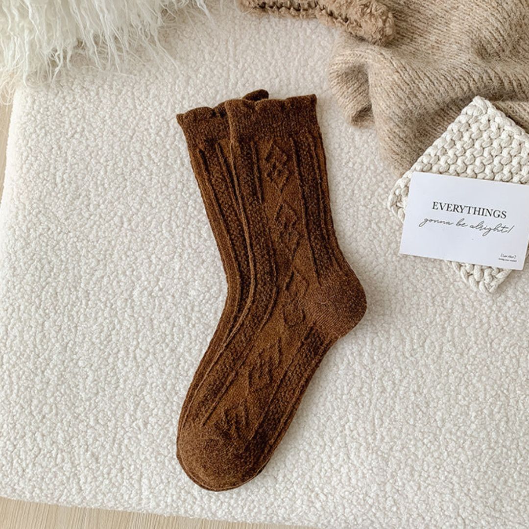 Braune Wollsocken mit Zopfmuster auf cremefarbener Decke, gemütliche Herbstmode.