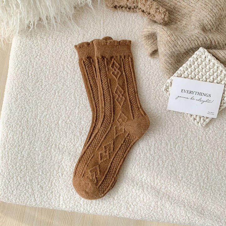 Braune Stricksocken mit Zopfmuster auf weißem Hintergrund, gemütliche Wintermode.