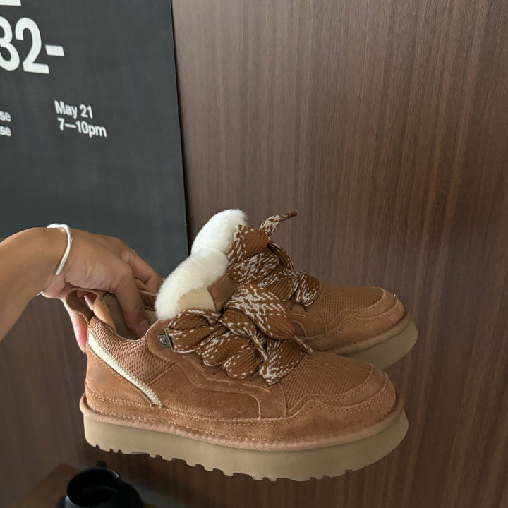 Braune Wildleder-Sneaker mit Fellfutter, handgehalten, vor Holzwand.
