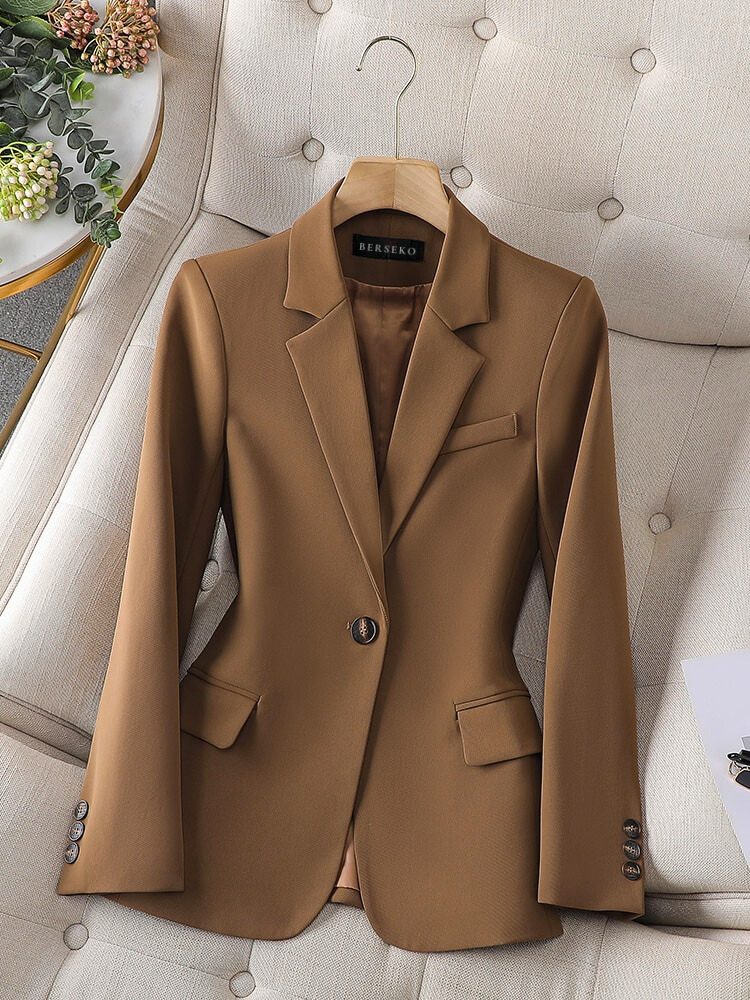 Eleganter brauner Damenblazer aus Wolle, einreihig, mit Knöpfen, auf beigem Sessel.