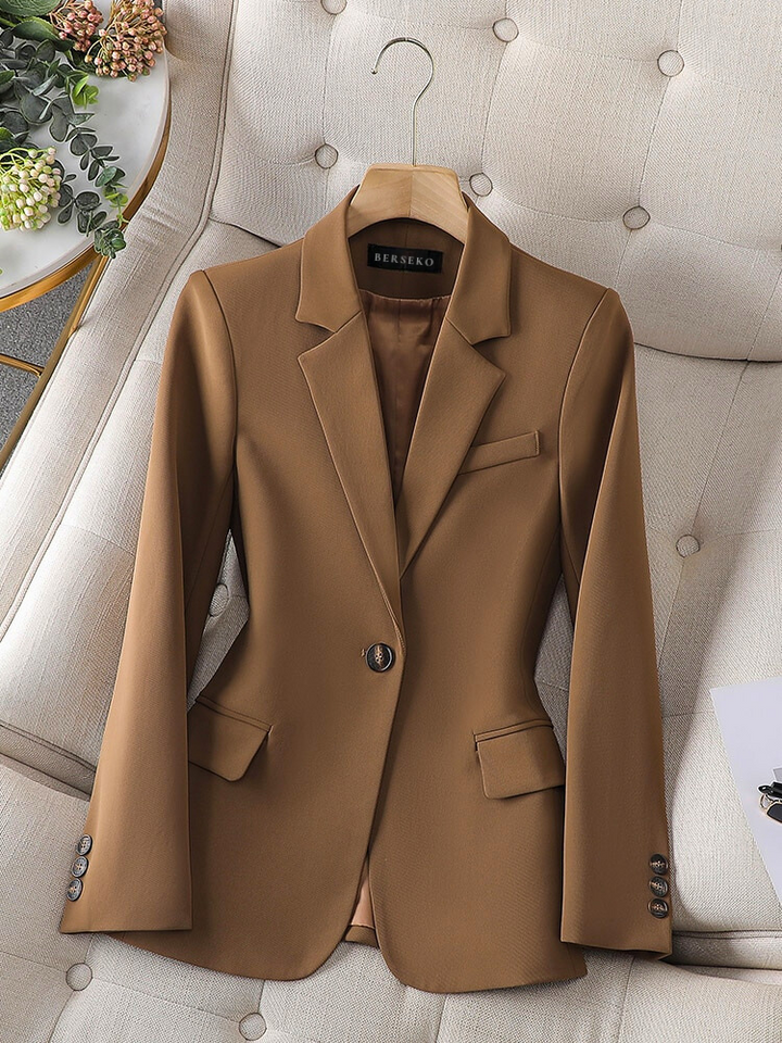 Eleganter brauner Damenblazer aus Wolle, einreihig, mit Knöpfen, auf beigem Sessel.