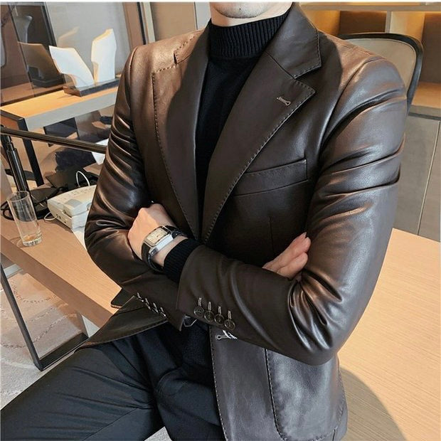 Mann in braunem Lederblazer, schwarzem Rollkragenpullover, sitzt mit verschränkten Armen.