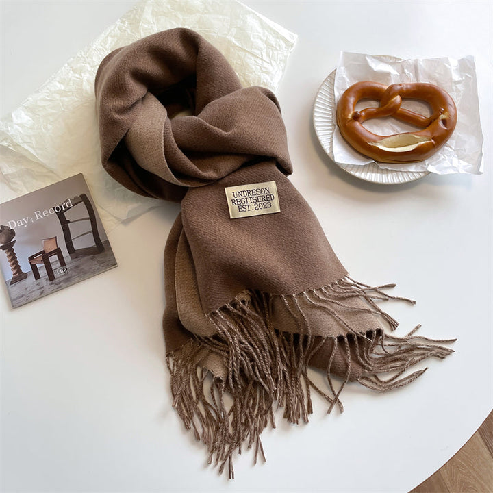 Brauner Wollschal mit Fransen, neben Brezel und Foto auf weißem Tisch.
