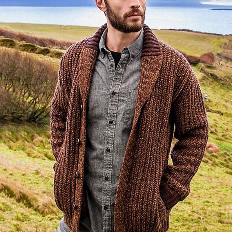 Mann in brauner Strickjacke und grauem Hemd in ländlicher Landschaft.