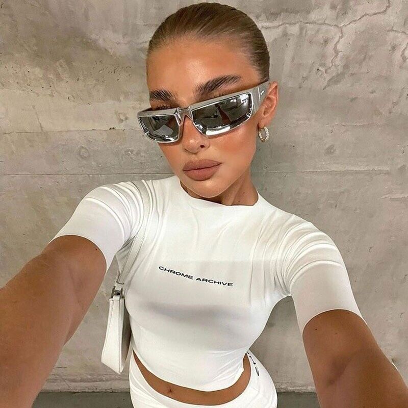 Frau in weißem Crop-Top mit Sonnenbrille, glattes Haar, modisches Outfit, Betonhintergrund.