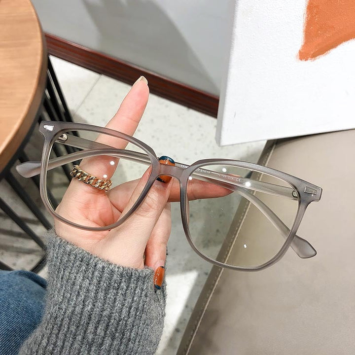 Graue, rechteckige Brille aus Kunststoff, modisch, unisex, Nahaufnahme, Hand hält Brille.