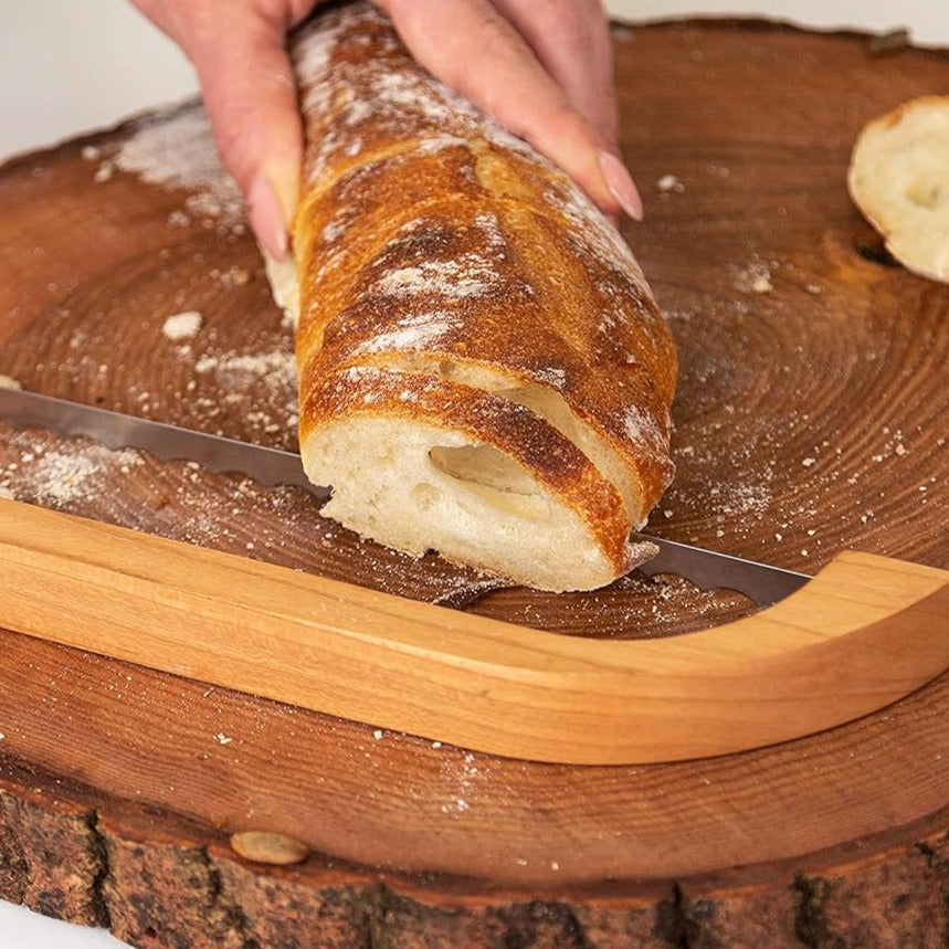 Hand schneidet Baguette auf rustikalem Holzbrett mit Brotmesser, Nahaufnahme.