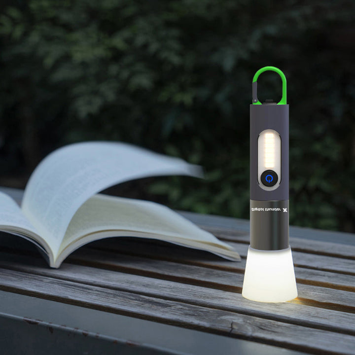 Tragbare LED-Laterne, schwarz, mit Haken, leuchtend, neben offenem Buch auf Holztisch.