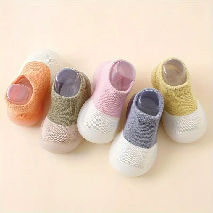 Fünf Paar bunte Babysocken aus Baumwolle, rutschfest, in Pastellfarben auf beigem Hintergrund.