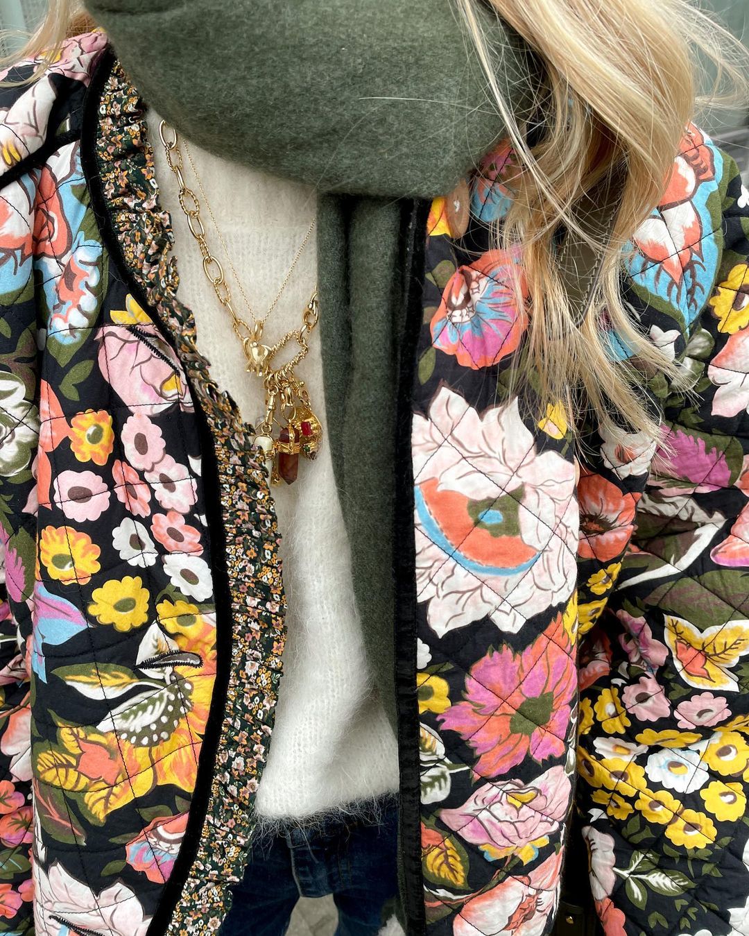 Frau mit bunter Blumenjacke, weißem Pullover und grünem Schal, modisches Herbstoutfit.