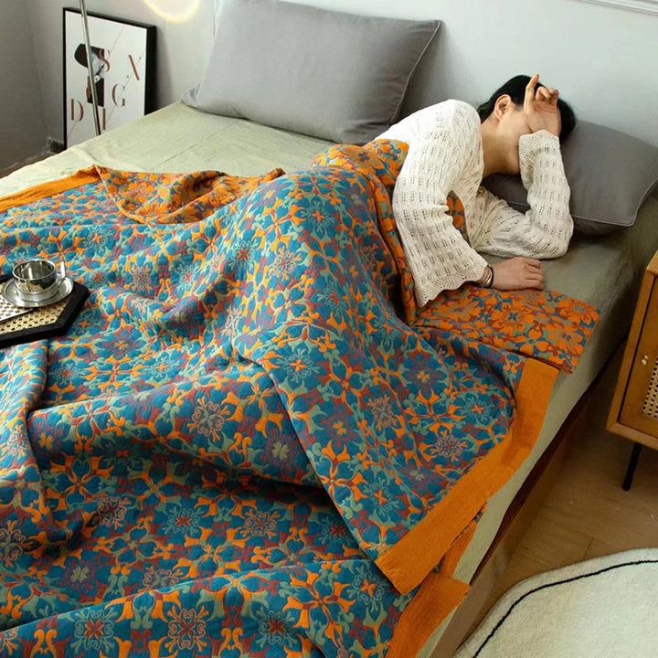 Person schläft unter bunter Blumenbettdecke auf grauem Bett, gemütliches Schlafzimmer, moderne Einrichtung.