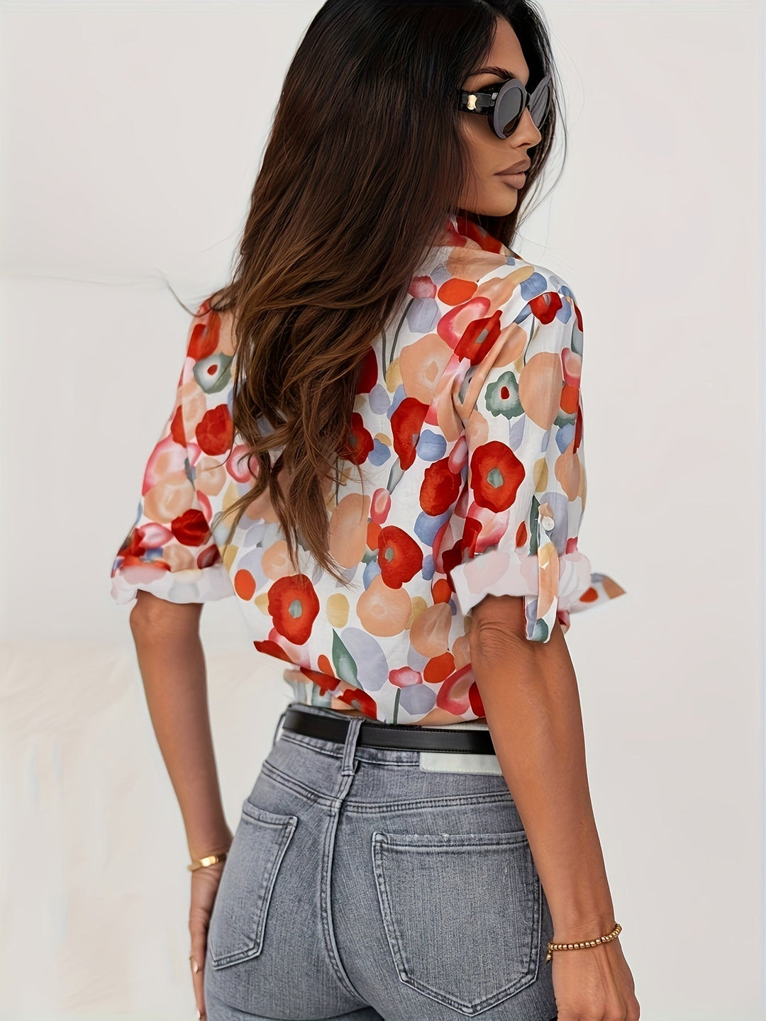 Frau in bunter Bluse mit Blumenmuster, Sonnenbrille, Jeans; modische Damenbekleidung.