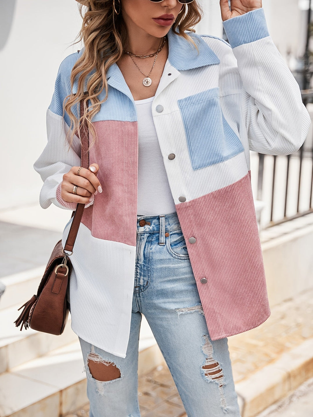 Frau in bunter Cordjacke, blau-weiß-rosa, mit brauner Tasche und zerrissenen Jeans.