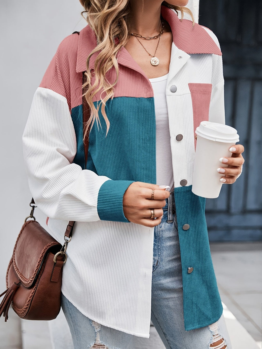Frau in bunter Cordjacke mit Kaffeebecher und brauner Umhängetasche, lässiger Streetstyle.