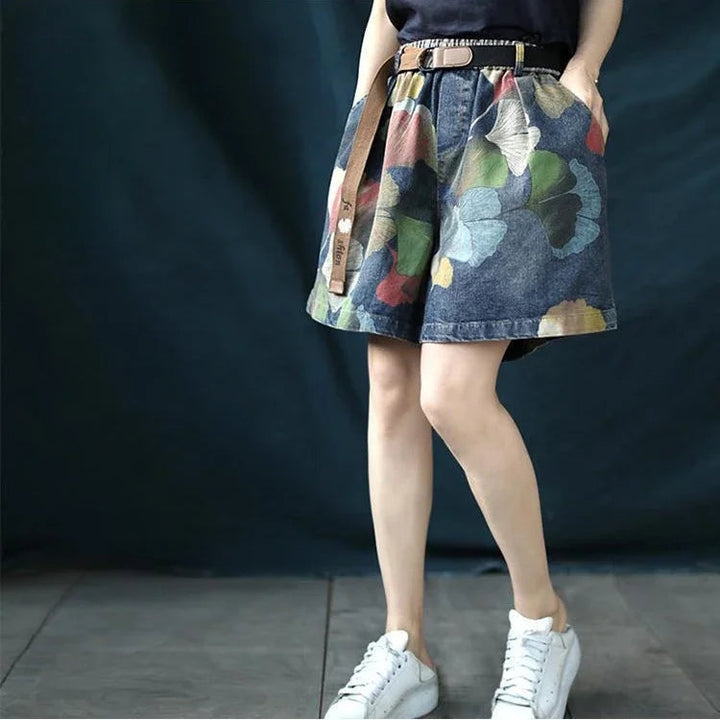 Frau trägt blauen Jeansrock mit Blumenmuster, Gürtel und weißen Sneakers.