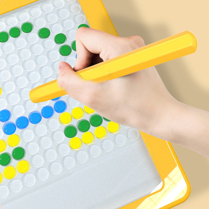 Hand hält gelben Stift auf magnetischem Mosaikbrett mit bunten Kreisen, Lernspielzeug.