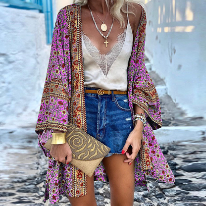 Frau in bunter Kimono-Jacke, Spitzen-Top, Jeansshorts, mit goldener Halskette und Clutch.