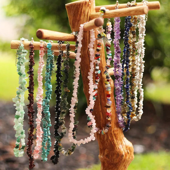 Verschiedene bunte Edelstein-Halsketten an Holzständer im Freien, Schmuck, Natursteine.