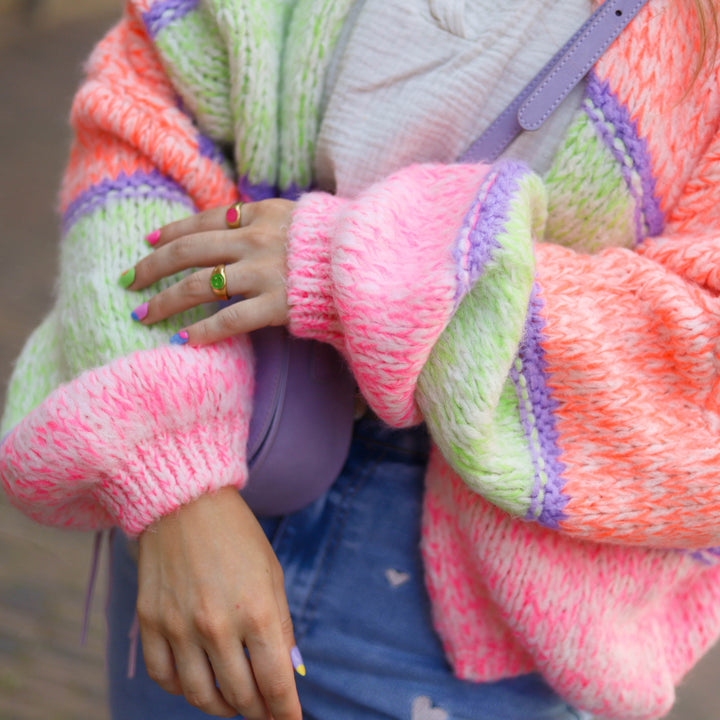 Frau in bunter Strickjacke, lila Tasche, Jeansrock, bunte Ringe und Nägel.