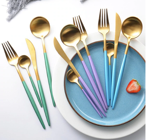 Goldenes Besteckset mit bunten Griffen auf blauem Teller, modernes Design, Edelstahl.