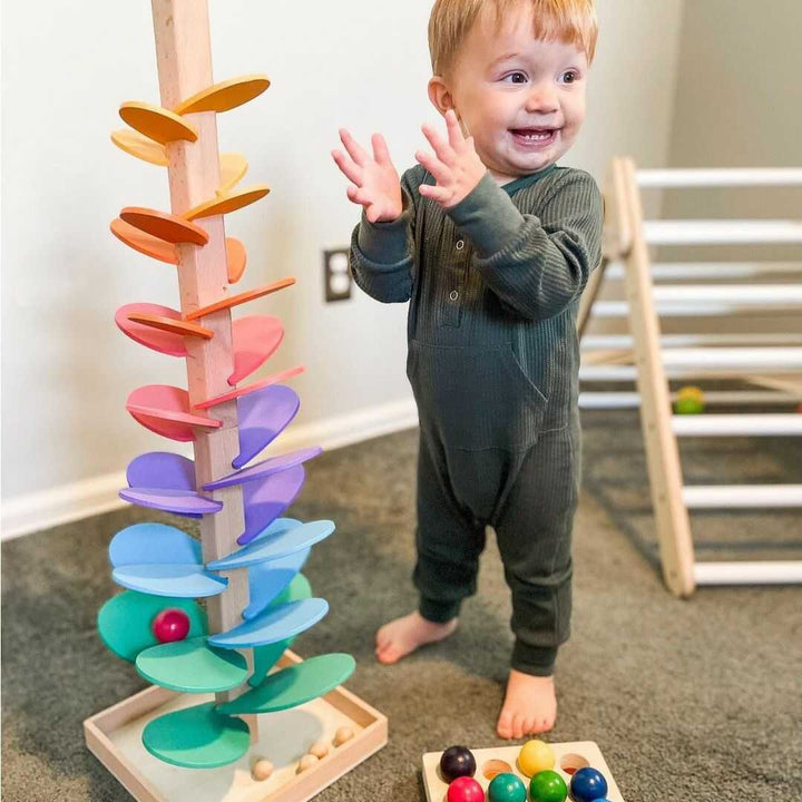 Kleinkind spielt mit buntem Holz-Murmelbaumspielzeug, Montessori, motorische Entwicklung.