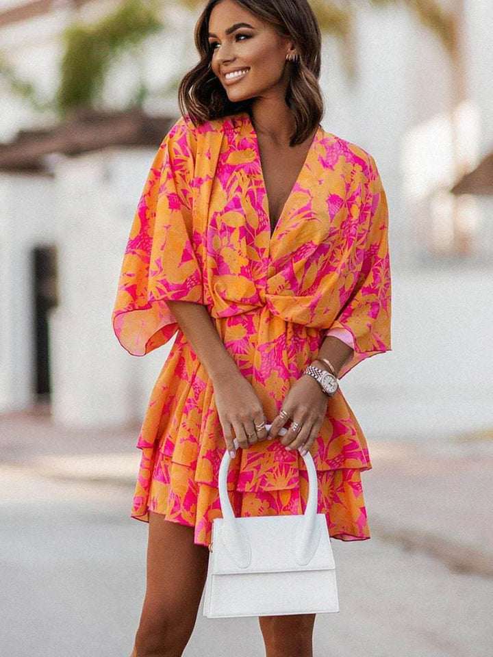 Frau in orange-pinkem Blumenkleid mit weißer Handtasche, Sommermode, lächelnd.