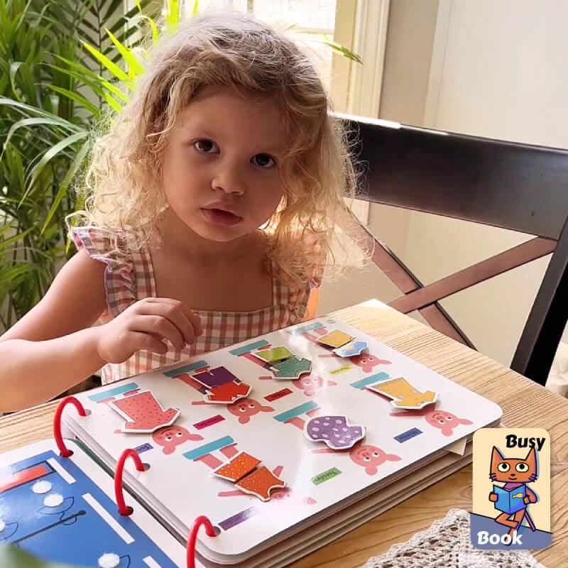 Kleinkind spielt mit Busy Book, sensorisches Lernbuch, farbenfrohe Formen, Tisch, Tageslicht.